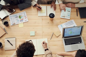 photo of office workers sitting around a table viewing multiple documents of charts and reports